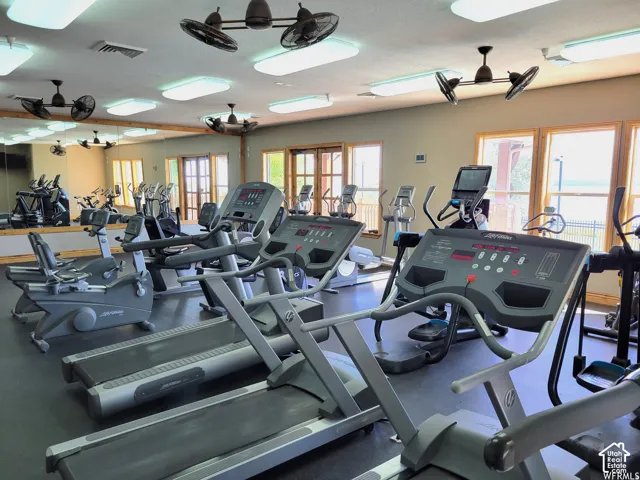 Fitness facility with multiple cardio machines, ceiling-mounted fans, recessed lighting, and expansive window openings