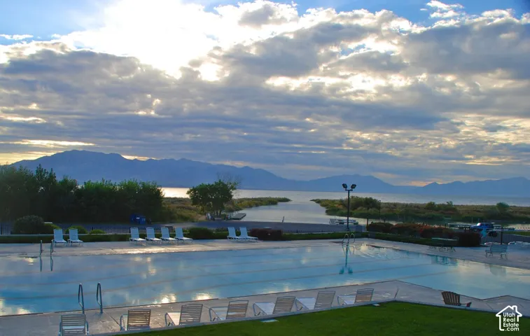 Expansive outdoor pool with a surrounding concrete deck, flanked by manicured green space, offering a mountain and water backdrop