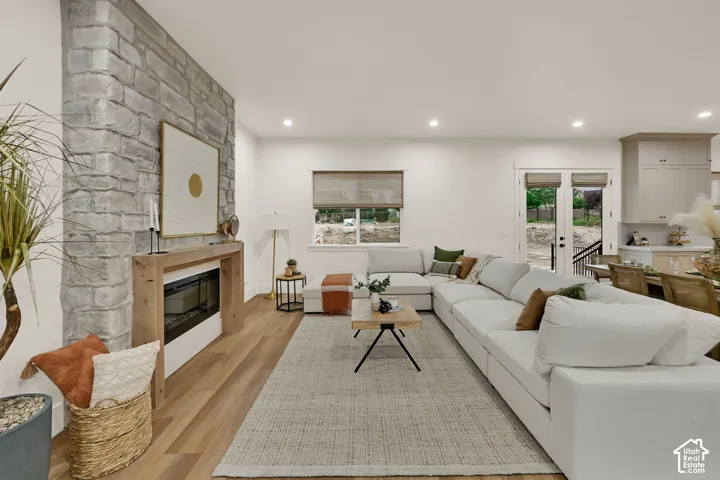 Expansive living area featuring stone-clad fireplace surround, wood-finish flooring, recessed lighting, and double glass panel doors