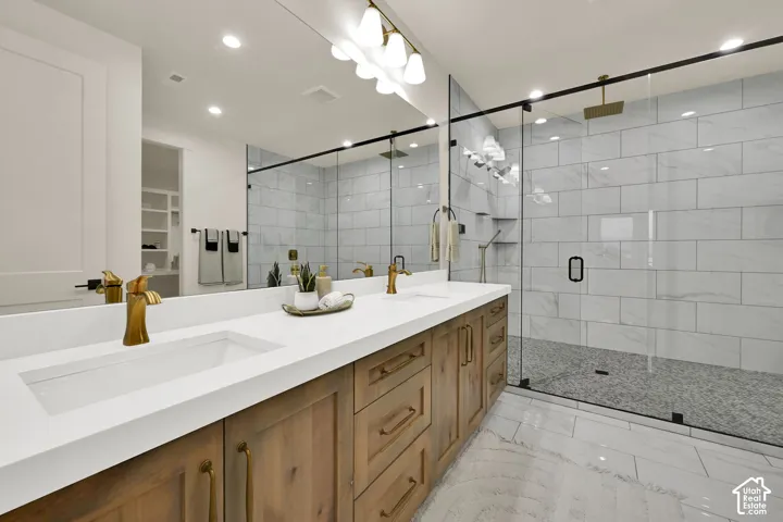 Dual vanity with integrated sinks, white countertops, wood-finish cabinetry, frameless glass shower enclosure, and large format floor tiling
