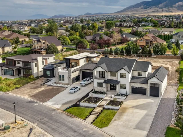 Aerial perspective of a modern two-story residence featuring a light-colored exterior, multi-car garage, and manicured landscaping with mature trees