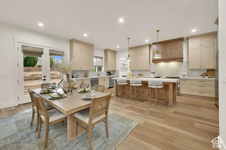Open-concept kitchen and dining area featuring wood-finish flooring, custom cabinetry, a built-in range hood, and a kitchen island with pendant lighting