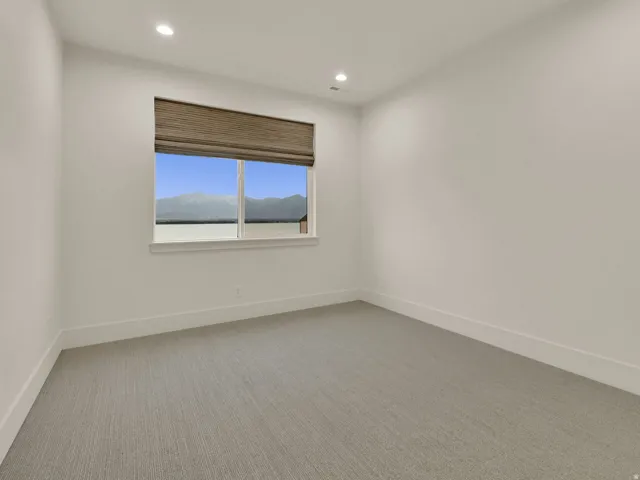 Recessed lighting, neutral wall paint, light-colored carpeting, window with mountain scenery, and a woven window treatment