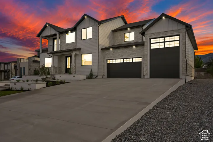 Modern-style exterior featuring stone and siding finishes, a covered entry, two balconies, and two attached garages with dark paneled doors