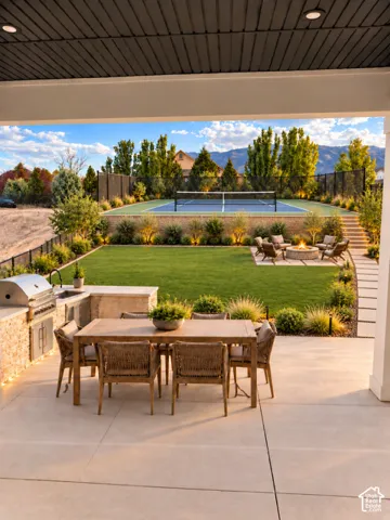 Expansive concrete patio with a built-in outdoor kitchen, manicured lawn, and a private sports court