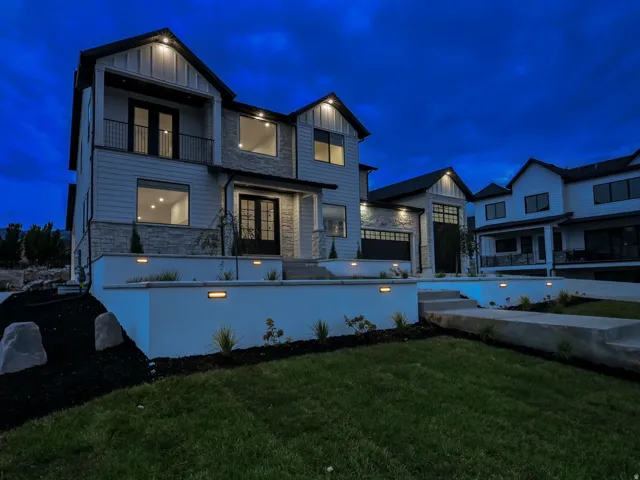 Modern architectural design with stone accents, integrated outdoor lighting, an attached garage, and a balcony with black railings