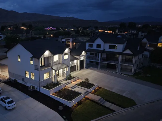 Modern exterior with stone and siding accents, illuminated landscaping, concrete driveway, and attached garage