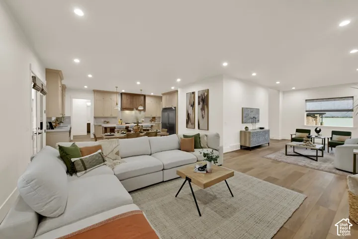 Open-concept living area with wood-finish flooring, recessed lighting, and a kitchen featuring light wood cabinetry