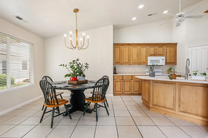Open-concept kitchen and dining area featuring wood-finish cabinetry, stainless steel appliances, tile flooring, a round pedestal dining table, and a brass chandelier suspended from a coffered ceiling