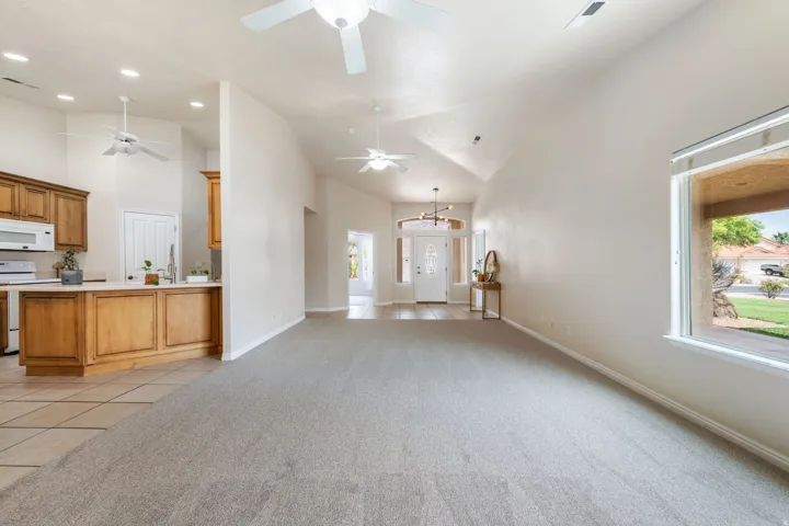 Open-concept living space featuring neutral tile flooring, vaulted ceilings with ceiling fans, recessed lighting throughout, and abundant natural light from large windows