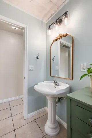 Elegant half bath featuring a classic pedestal sink with chrome fixtures, wood-framed mirror with decorative top detail, and soft blue-gray wall finishes