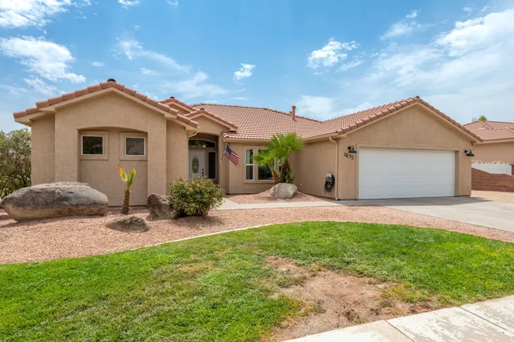 Stucco exterior with clay tile roofing and arched entryway, complemented by mature desert landscaping and river rock hardscaping