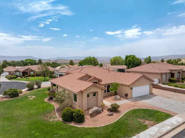 Stucco exterior with a terracotta tile roof, attached two-car garage, and a manicured lawn