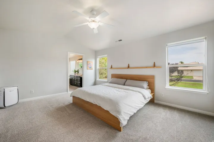 Vaulted ceiling with a ceiling fan, light gray carpeting, and two bright windows