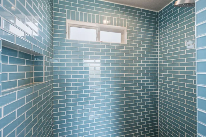 Shower enclosure with blue subway tile, an integrated shower niche, and a fixed window