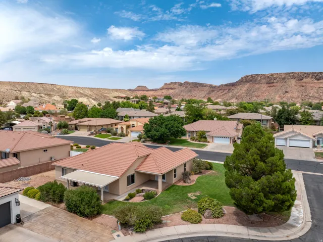 Scenic desert foothill setting with sprawling single-story residence featuring a terracotta tile roof, stucco exterior, and mature landscaping including evergreen trees and manicured grounds