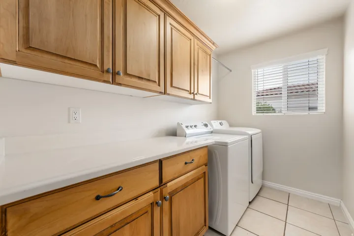 Dedicated laundry room featuring custom wood cabinetry with ample storage, white quartz countertops, tile flooring, and side-by-side washer and dryer hookups