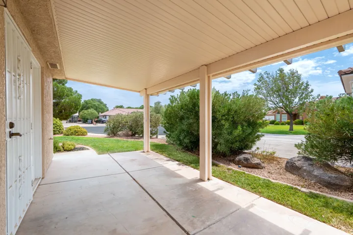 Covered concrete patio with decorative security door, surrounded by landscaped plantings and natural rock features