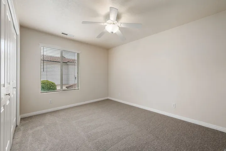 Recessed window with horizontal blinds, neutral-toned walls, gray-toned carpeting, and a ceiling fan with integrated lighting