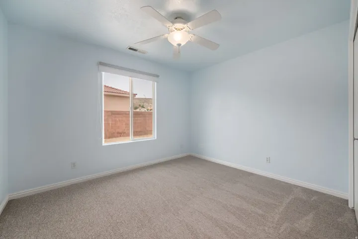 Bright bedroom featuring soft blue walls, neutral carpet flooring, and a ceiling fan with integrated lighting