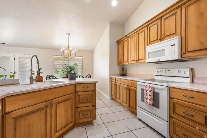 Spacious kitchen featuring warm wood cabinetry, tile flooring, stainless steel appliances including a white microwave and electric range, white subway tile backsplash, and an island with seating