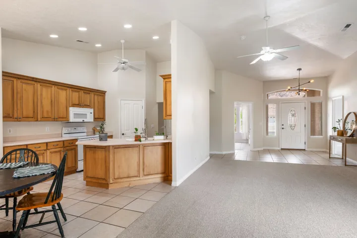 Open-concept kitchen and living area featuring wood cabinetry, tile flooring, recessed and pendant lighting, and ceiling fans throughout