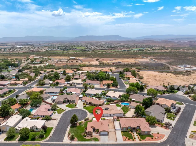Aerial view showcasing this residential community nestled within a sprawling valley landscape, featuring single-story homes with terracotta tile roofing, manicured lawns, mature trees, and paved streets throughout the established neighborhood