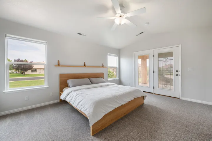 Spacious primary bedroom with wood-finish bed frame, ceiling fan with integrated lighting, carpeted flooring, and abundant natural light from large picture window