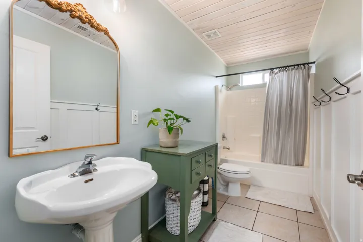 Bright, updated bathroom featuring a pedestal sink with chrome faucet, wood-framed mirror, tile flooring, and a shower-tub combination with curtain rod