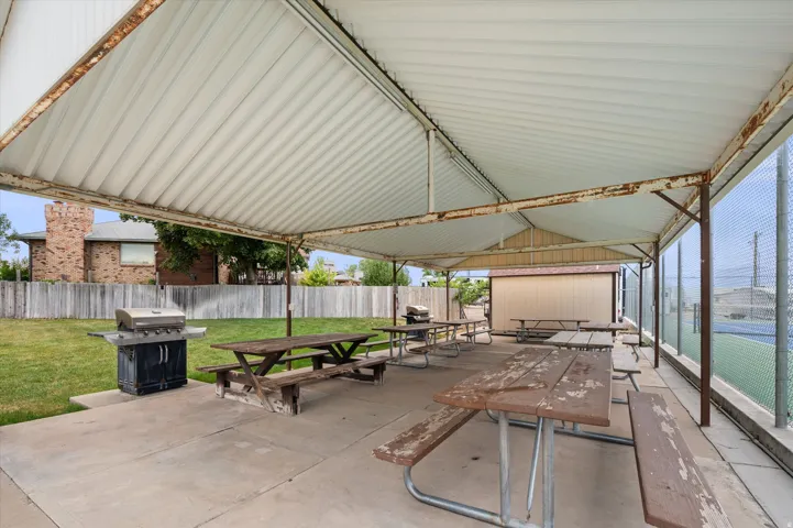 Covered outdoor patio with concrete flooring, multiple picnic tables, and a gas grill