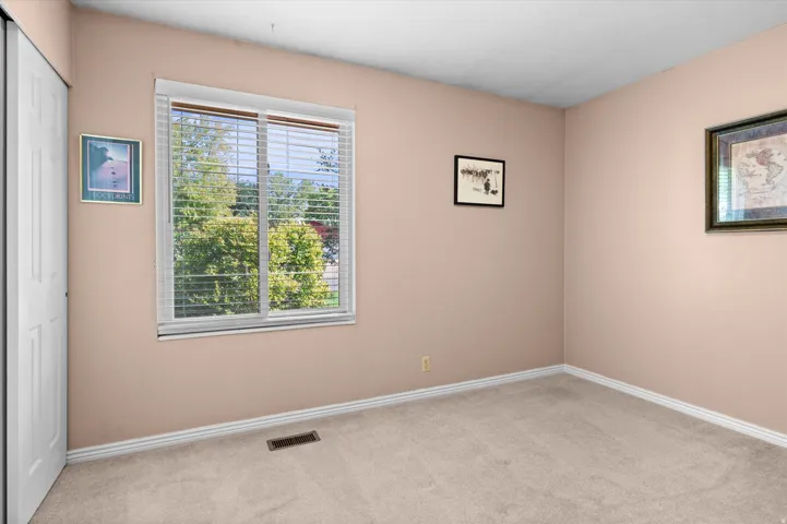 Bright secondary bedroom offering neutral wall finishes, neutral carpet flooring, and abundant natural light from a large double-hung window with horizontal blinds