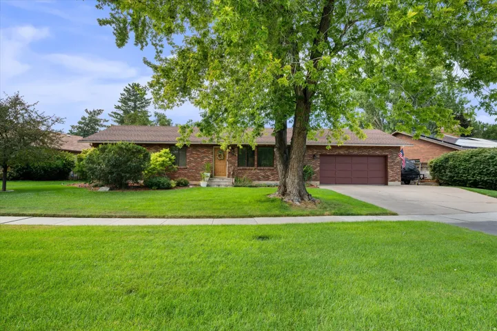 Brick exterior with a traditional brown shingle roof, attached garage, concrete driveway, and mature landscaping