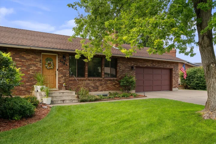 Brick exterior with a brown shingle roof, attached two-car garage, concrete driveway, and established front landscaping
