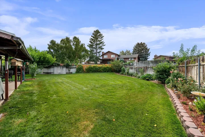 Expansive backyard featuring a manicured lawn bordered by mature trees and established landscaping