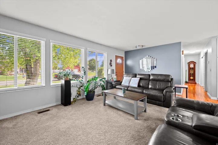 Bright, light-filled living room featuring expansive windows with natural greenery views, neutral carpet flooring, and a blue accent wall