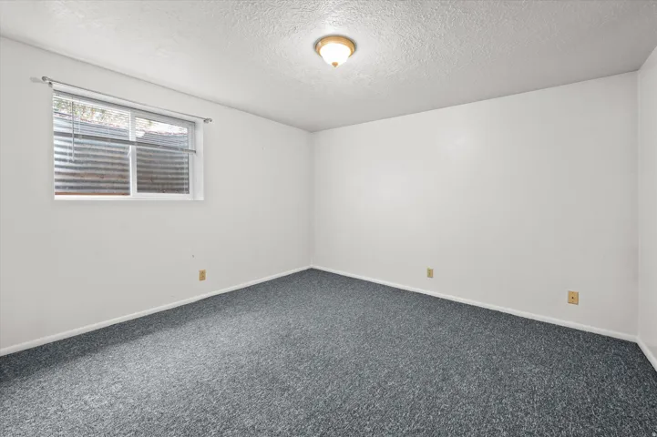 Spacious bedroom featuring neutral wall finishes, carpeted flooring, dual window with blinds providing natural light, and multiple electrical outlets for convenient placement of furnishings