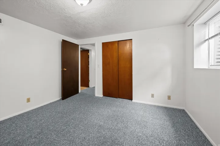 Spacious bedroom featuring neutral wall finishes, gray carpet flooring, wood-finish closet doors, and abundant natural light from a corner window