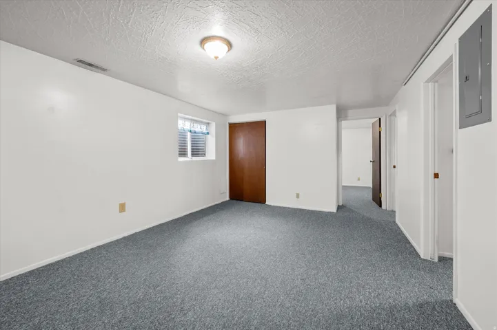 Spacious basement room featuring neutral wall finishes, carpeted flooring, recessed ceiling lighting, and a solid wood entry door