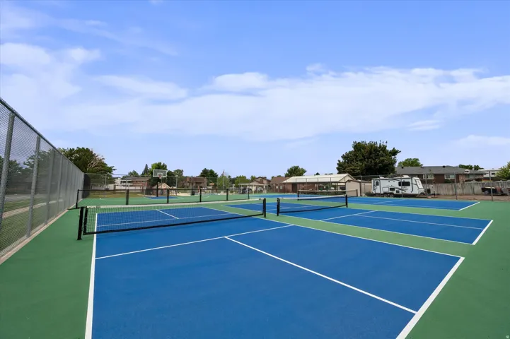 Multiple hard surface courts, blue and green playing surfaces, black court nets, and perimeter fencing