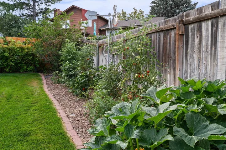 Lush garden bed with mature plants, wood privacy fencing, and a brick-edged border