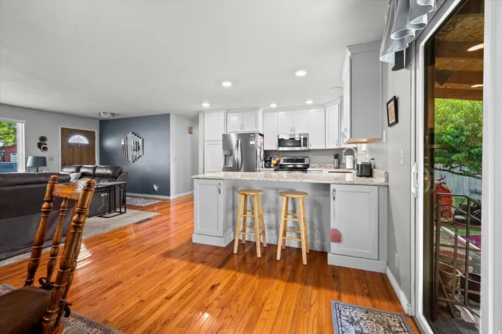 Open-concept kitchen and dining area featuring white cabinetry, stainless steel appliances, wood-finish flooring, and a central island with seating