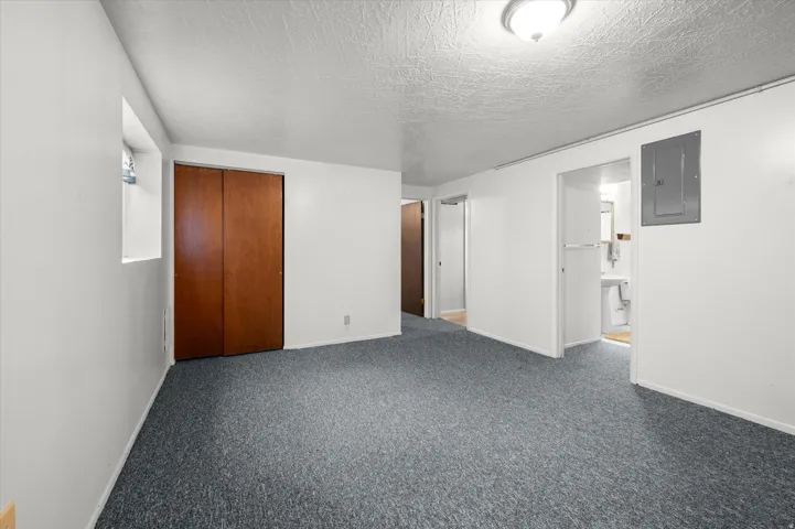 Textured ceiling, wall-mounted light fixture, gray-toned carpeting, and a window opening