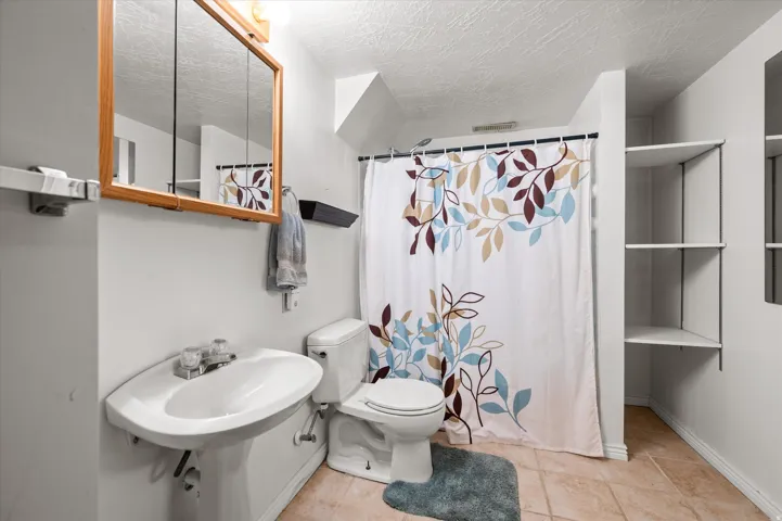 Full bathroom featuring a pedestal sink with chrome fixtures, toilet, tile flooring, and a shower/tub combination with decorative shower curtain