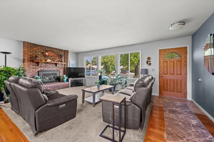 Spacious living room anchored by a wood-burning fireplace with brick surround and mantelpiece, complemented by large multi-pane windows offering natural light