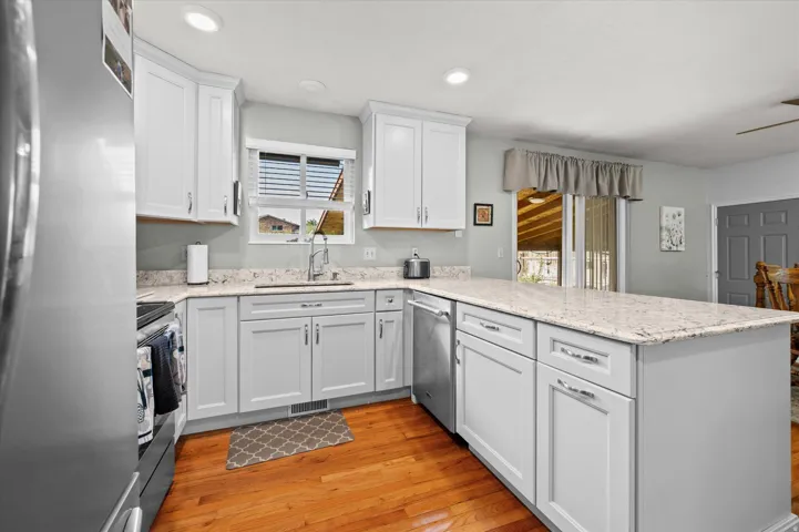 Hardwood flooring, kitchen island with built-in storage, white upper and lower cabinetry, stainless steel appliances, and a window above the sink