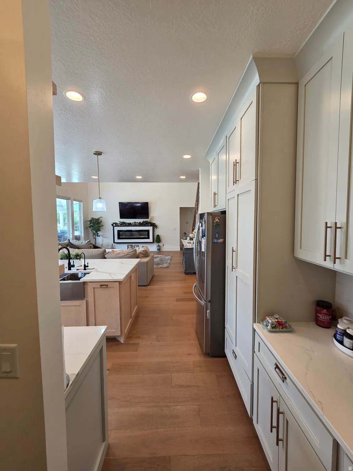 Galley-style kitchen featuring white cabinetry, stainless steel appliances, wood-finish flooring, recessed ceiling lighting, and ample counter and storage space with a pass-through opening to the adjoining living area