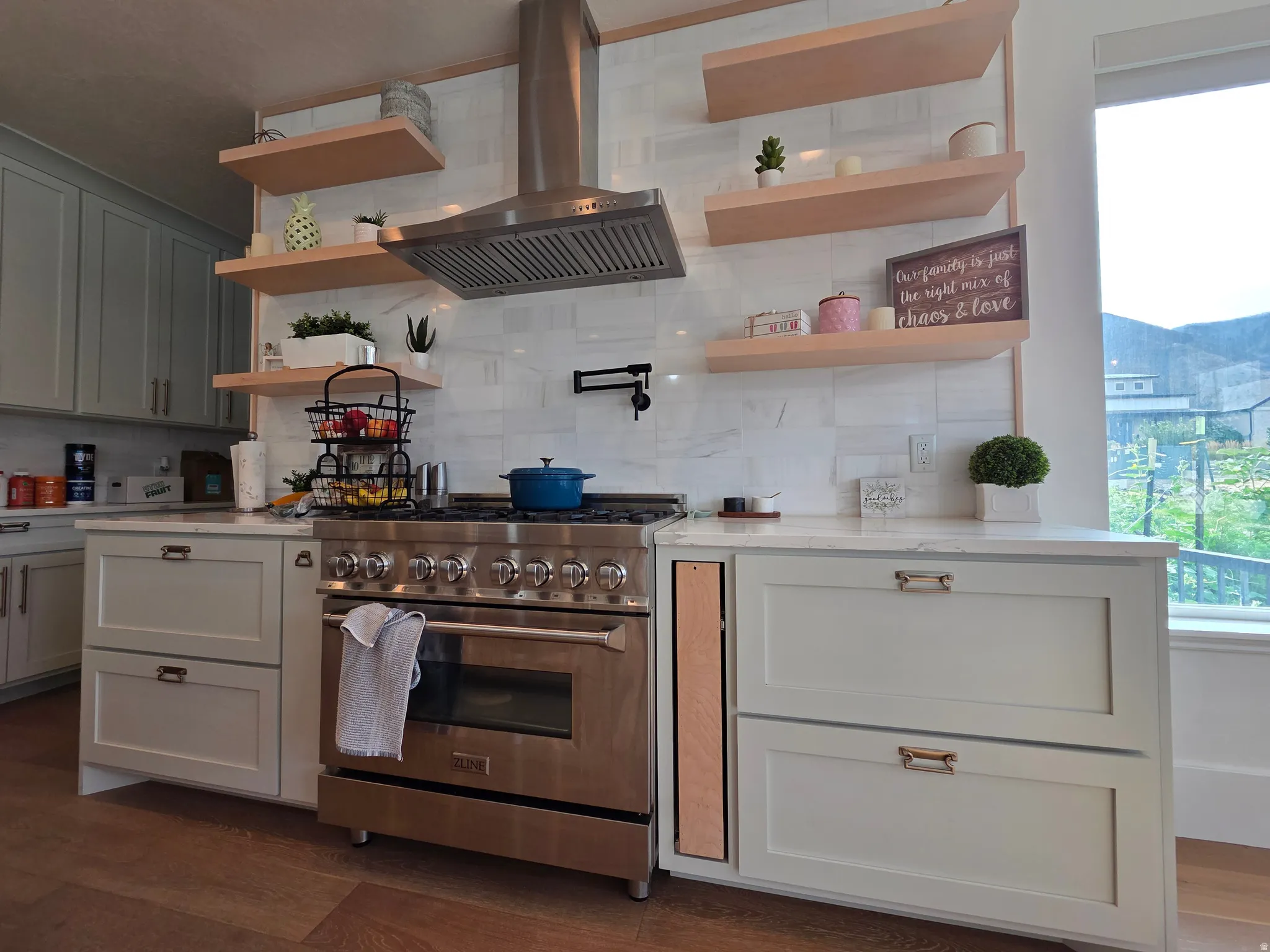 Modern kitchen featuring a professional-grade dual-fuel range with six burners and convection oven, custom cabinetry with soft-close drawers, floating wood-finish shelving with integrated storage, quartz countertops, stainless steel range hood, and abunda