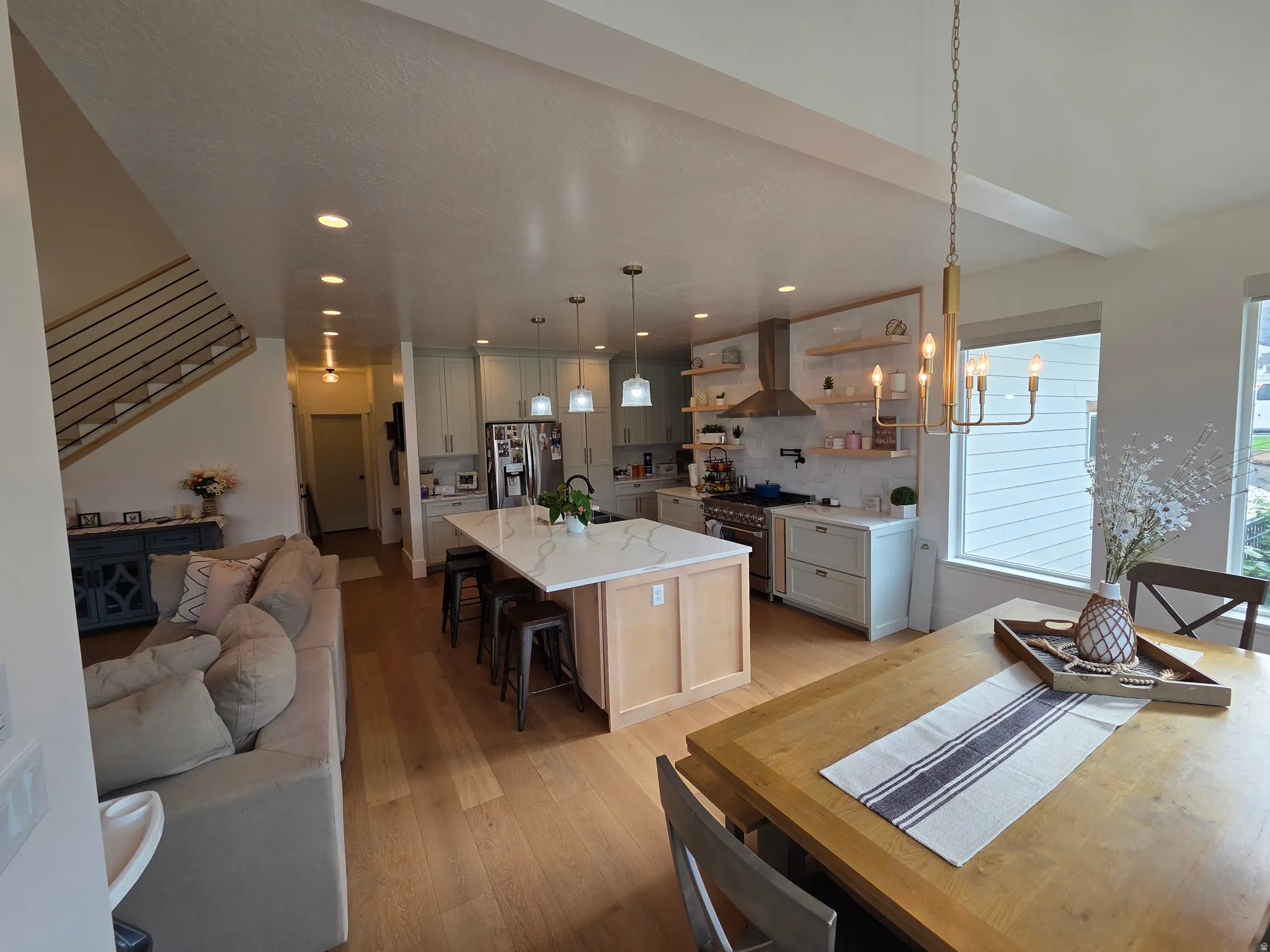 Open-concept kitchen and dining area featuring a large center island with seating, white cabinetry, stainless steel appliances, and wood-finish flooring throughout