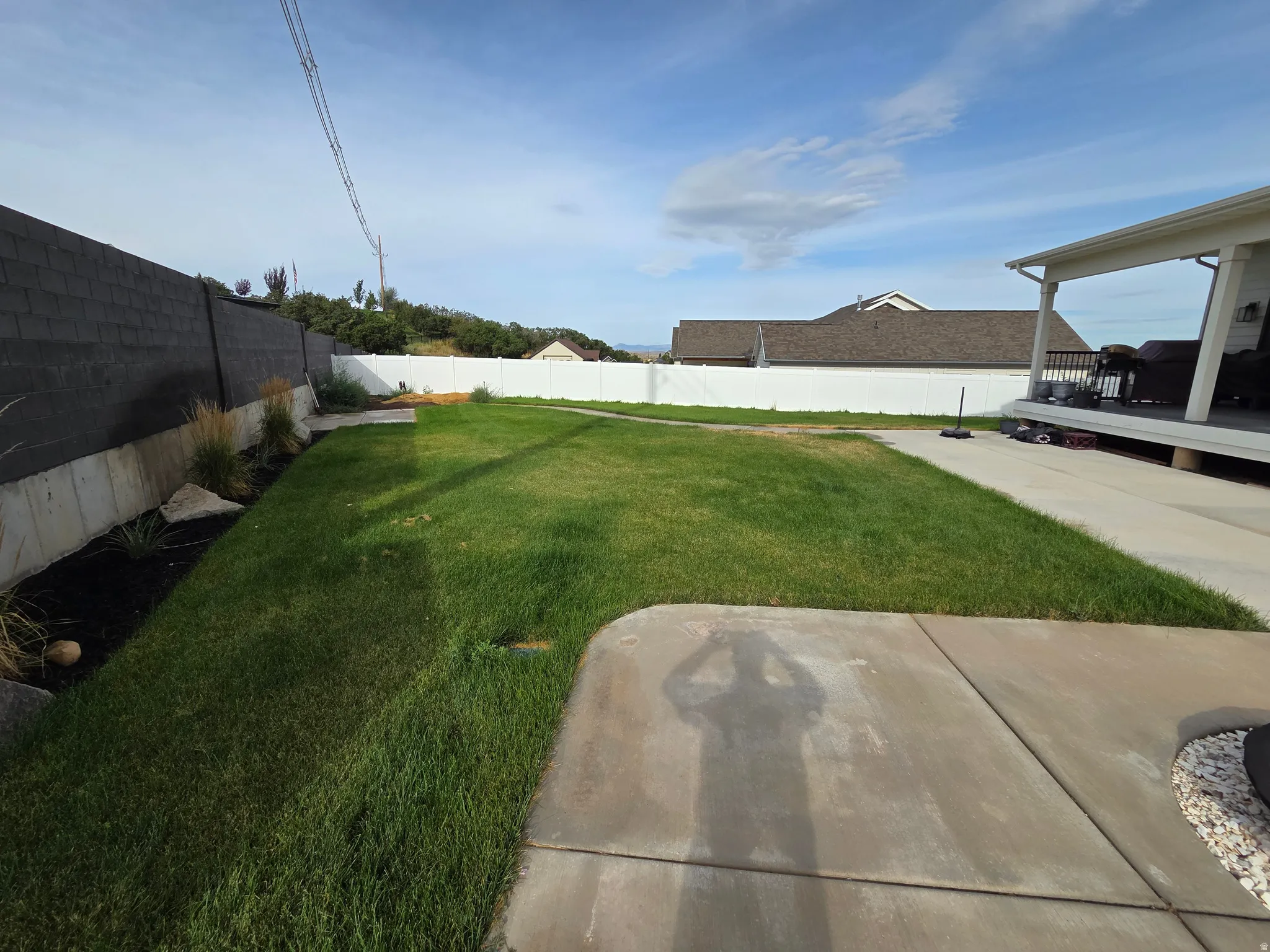 Expansive backyard featuring a manicured lawn, concrete patio, and a covered porch