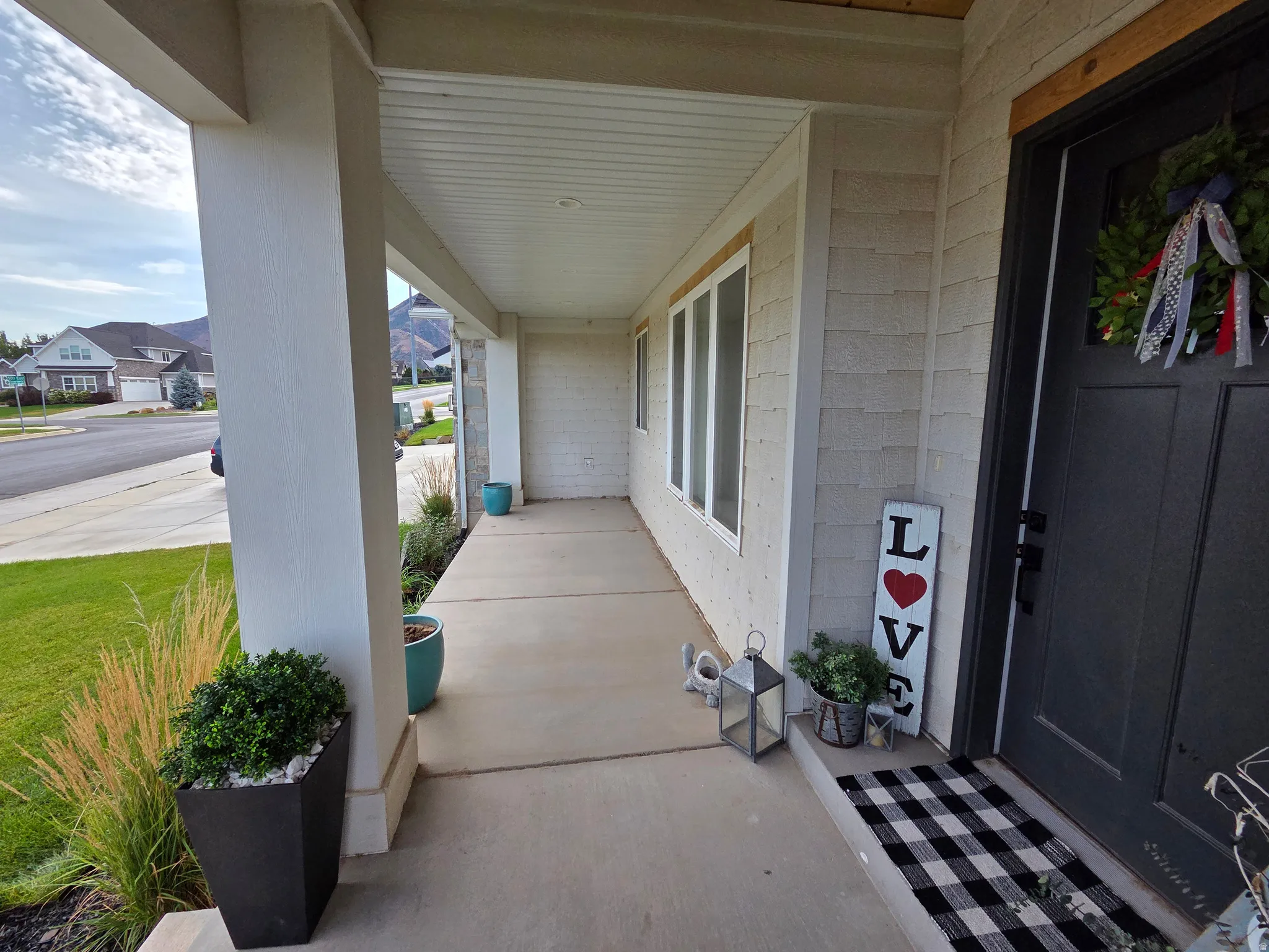Welcoming front porch featuring covered entry with white painted columns, concrete flooring, and black painted entry door with sidelights